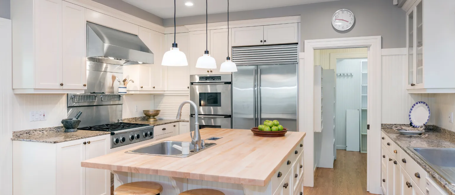 After kitchen remodeling project in Los Angeles with custom white cabinets, large kitchen island, stainless steel appliances, pendant lighting, and improved storage layout